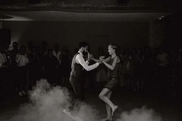 Couple dansant dans une ambiance brumeuse et monochrome, entouré d'invités, lors d'une soirée élégante.