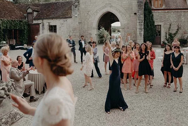 Invités joyeux célébrant un mariage dans la cour d'un château, avec une femme en robe bleue dansant avec enthousiasme.
