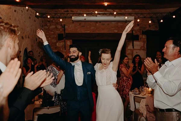 Jeunes mariés rayonnants dansant avec joie entourés de leurs invités lors d'une réception chaleureuse.