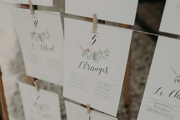 Cartes de placement de table blanches avec calligraphie et motifs végétaux, suspendues à un fil doré.