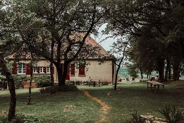 Maison de campagne aux volets rouges entourée d'arbres et d'un jardin verdoyant pour un mariage bohème et champêtre.