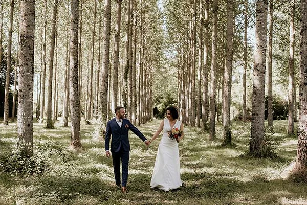 Jeunes mariés main dans la main marchant dans une forêt de peupliers lumineuse, ambiance champêtre et romantique.