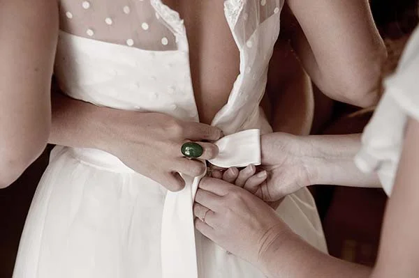 Gros plan sur des mains aidant une mariée à ajuster sa robe blanche minimaliste et moderne.