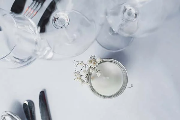 Composition minimaliste et lumineuse de verres à pied, couverts et bougie blanche ornée de gypsophile.