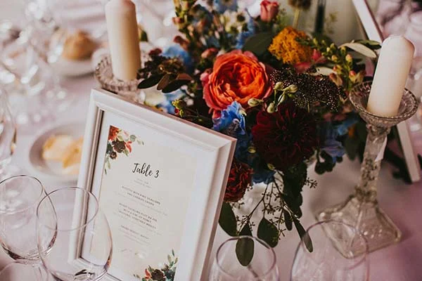 Centre de table coloré avec fleurs variées, bougies blanches et marque-place Table 3 pour un mariage champêtre.