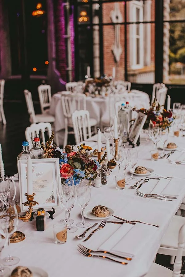 Table de mariage élégante avec nappe blanche, fleurs colorées et décoration raffinée dans un cadre lumineux.