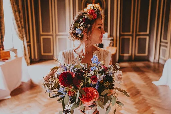 Mariée de profil avec couronne et bouquet de fleurs colorées dans un intérieur élégant au style classique.