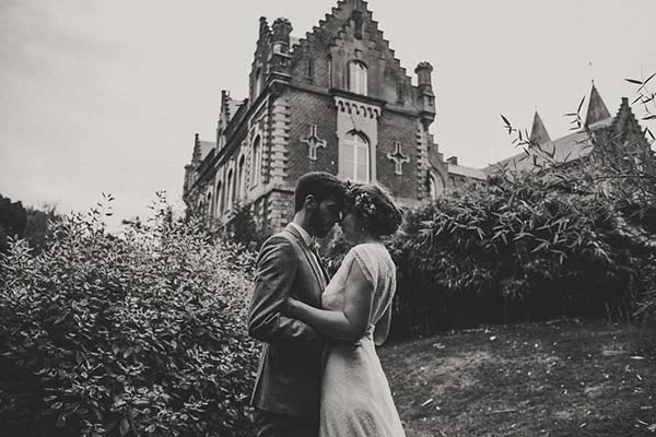 Couple de mariés s'embrassant devant un château belge dans une ambiance romantique, cliché en noir et blanc.