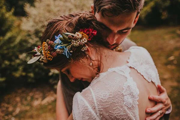 Couple enlacé, la mariée portant une couronne de fleurs colorées et une robe en dentelle blanche, ambiance champêtre.