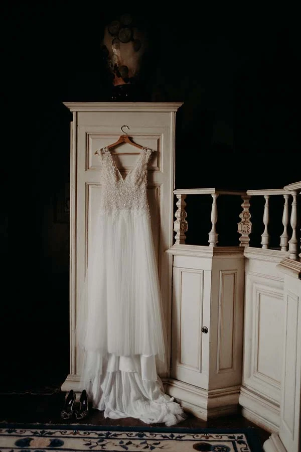 Robe de mariée blanche et élégante suspendue à un meuble ancien, avec des escarpins noirs à ses pieds.