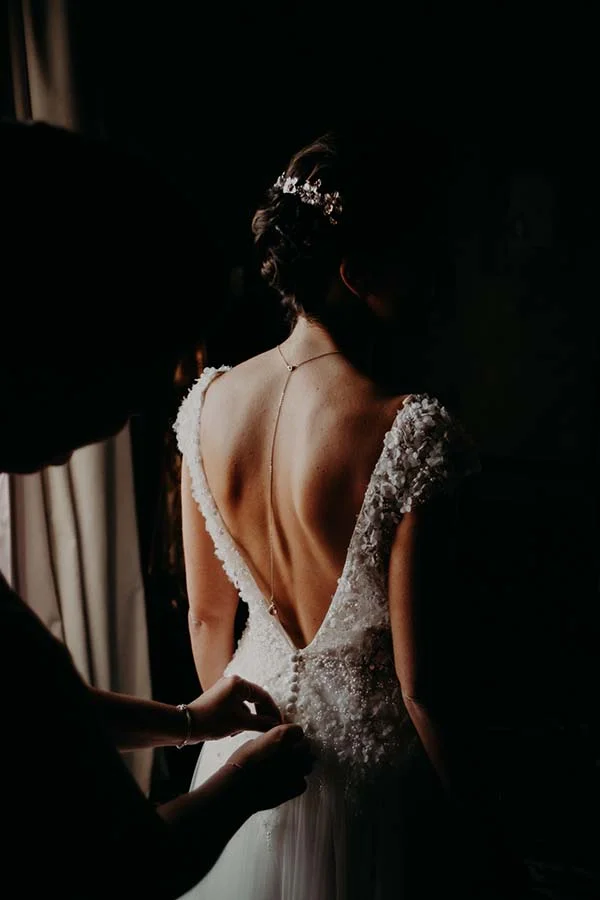 Vue de dos d'une mariée en robe blanche et diadème, éclairée en clair-obscur dans une ambiance chic et intimiste.