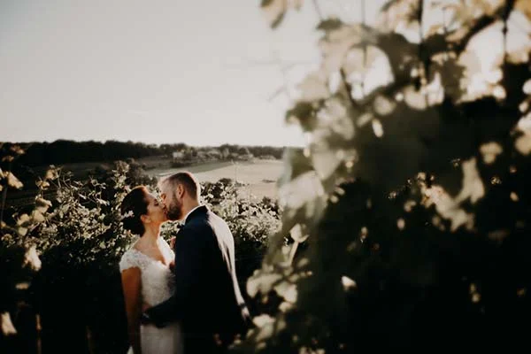 Jeunes mariés s'embrassant avec tendresse dans un paysage naturel baigné d'une lumière dorée et romantique.
