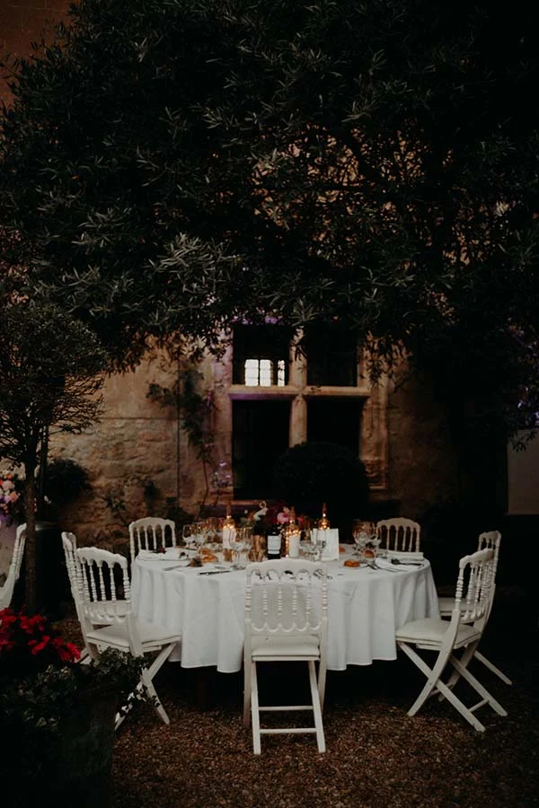 Table ronde élégante dressée pour un dîner de mariage sous un olivier, dans une ambiance nocturne et romantique.