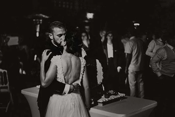 Couple de mariés s'embrassant avec tendresse lors d'une réception chic, cliché artistique en noir et blanc.