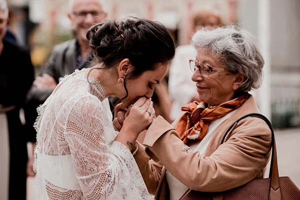 Une mariée en robe de dentelle blanche embrasse tendrement la main d'une femme âgée lors d'un mariage romantique.