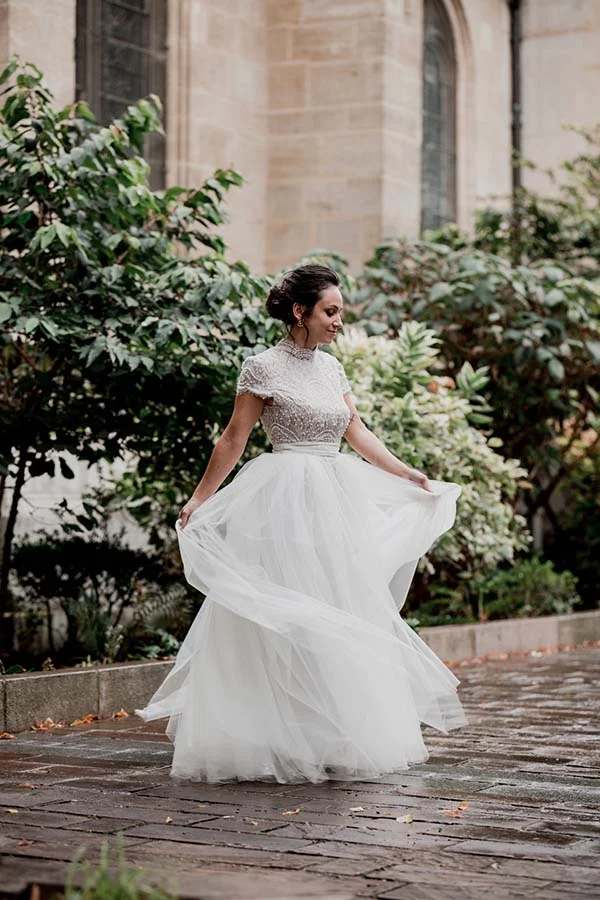 Une mariée en robe blanche vaporeuse et haut perlé tournoie avec élégance dans un jardin romantique.