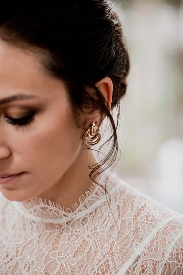 Gros plan profil d'une mariée en robe de dentelle blanche avec des boucles d'oreilles dorées, ambiance romantique.