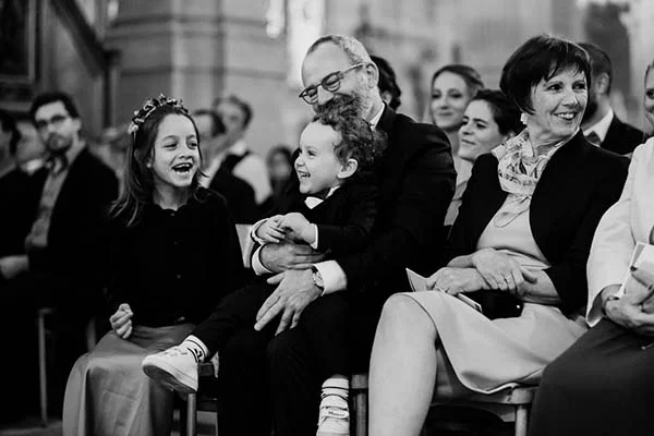 Famille souriante et élégante, dont deux enfants, assistant à une cérémonie de mariage en noir et blanc.