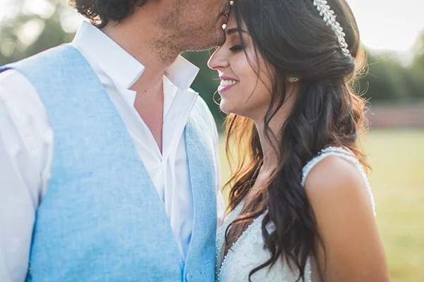 Jeune couple marié s'enlaçant tendrement en extérieur, portant un gilet bleu ciel et une robe blanche élégante.