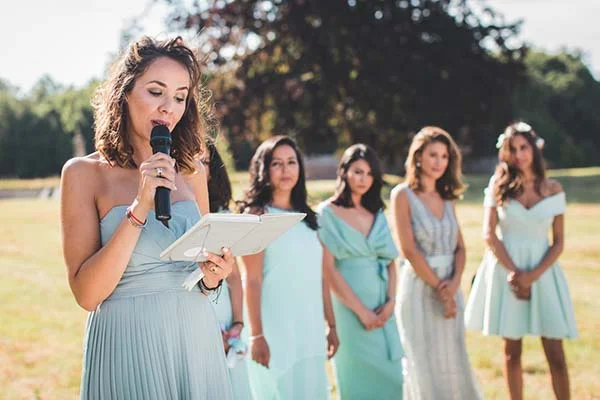 Une demoiselle d'honneur en robe bleu pastel prononce un discours devant ses amies lors d'un mariage champêtre.