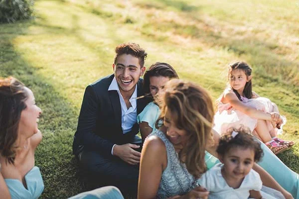 Un groupe d'invités élégants rit et discute, assis dans l'herbe lors d'un mariage chic et champêtre.