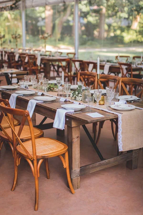 Table de mariage chic et champêtre en bois avec chaises crossback, dressée avec élégance sous un chapiteau transparent.
