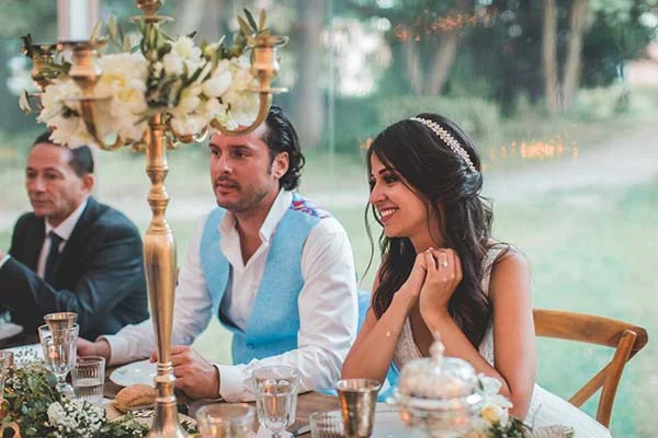 Jeunes mariés souriants à une table chic et champêtre, avec un candélabre doré et des fleurs blanches.