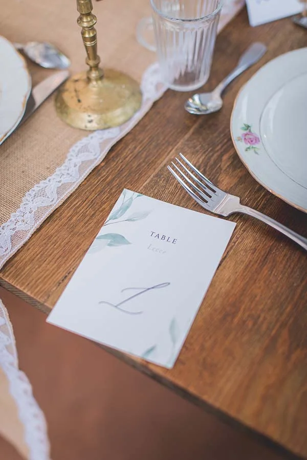Détail d'une table de mariage chic et champêtre avec un marque-place élégant, de la dentelle et de la vaisselle fleurie.