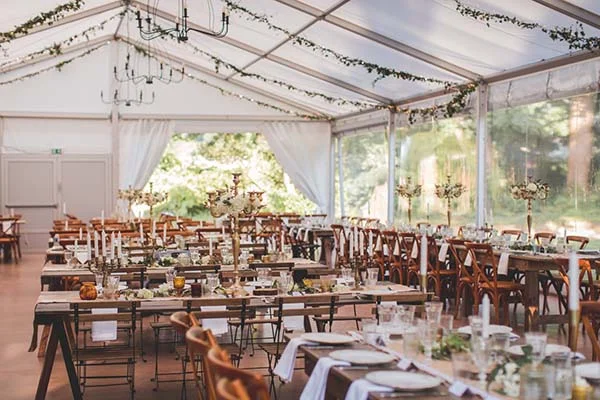 Réception de mariage chic et champêtre sous un chapiteau blanc avec tables en bois, fleurs blanches et chaises bistrot.