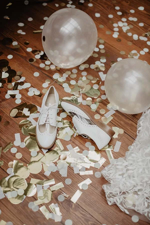 Chaussures blanches délicates et décoratives sur les parquets, décorées de confettis et de ballons, pour une ambiance