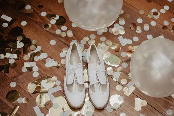 Éclatante paire de chaussures blanches et dorées, décorées de confettis et de ballons, pour une journée de mariage inoubliable.