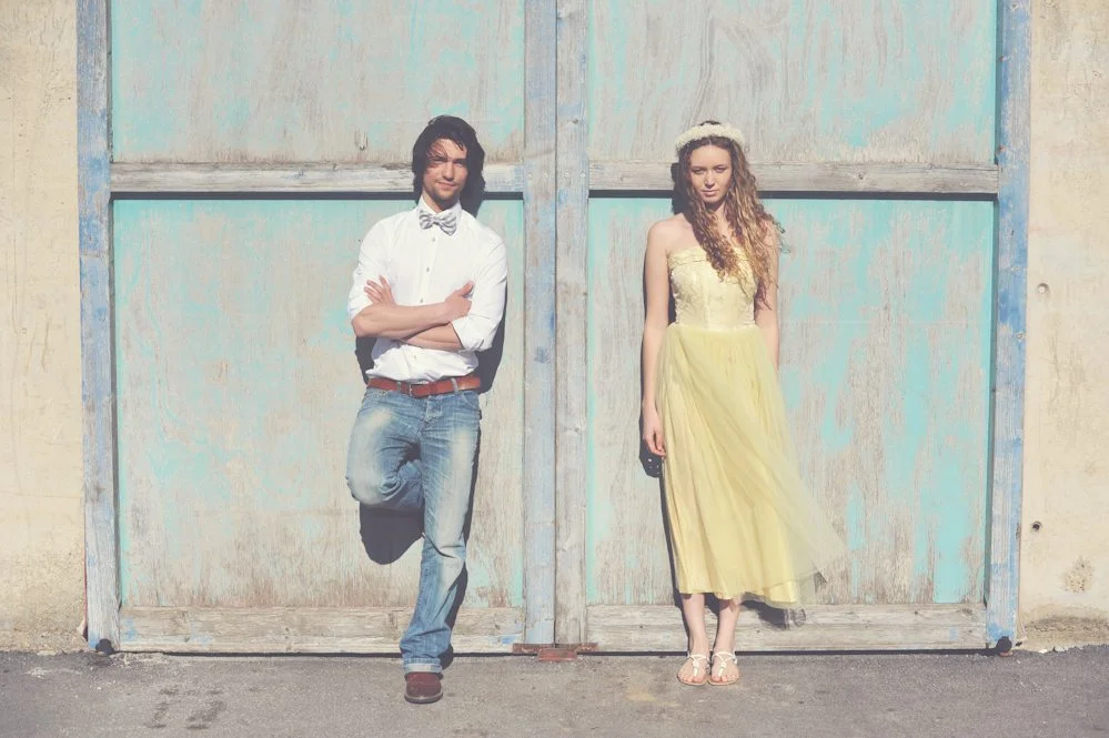 Un couple charmant debout devant une porte peinte, l'homme dans un chemisier blanc et jeans, l'homme dans un jupe