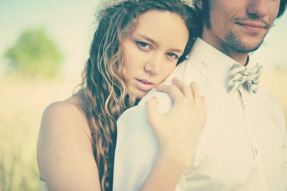 Un couple romantique se pose dans un champ, l'homme en chemise blanche et cravate à rayures, la femme en robe blanche