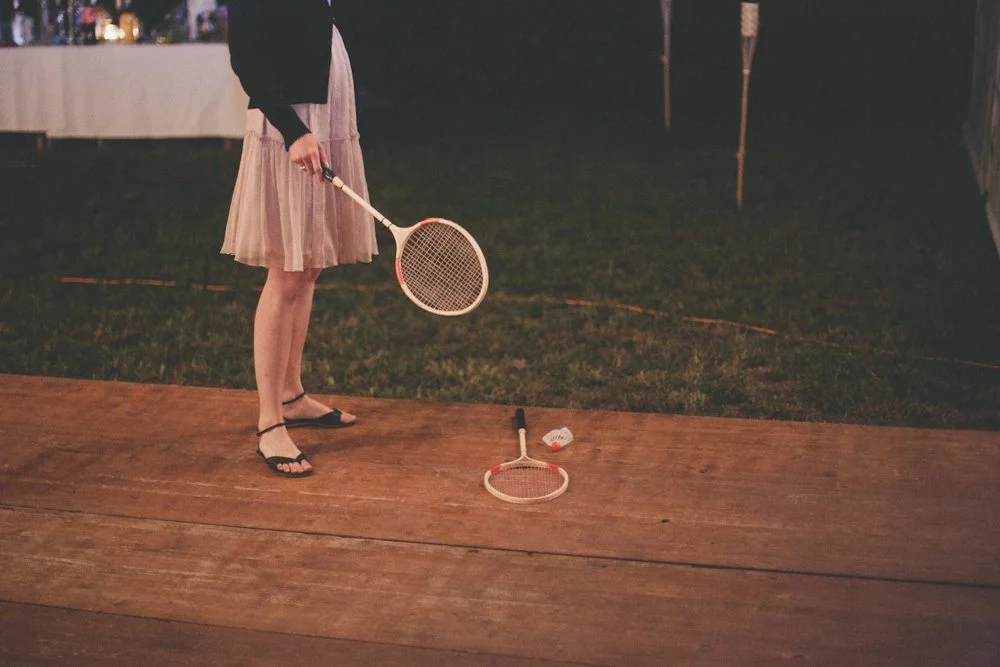 Une jeune femme dans un joli robe de soirée et des sandales noires tient un raquette de badminton, prêt à se lancer