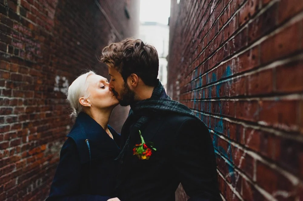 Un couple romantique partage un baiser tendre dans un passage de briques rouges, incarnant l'ambiance intime et