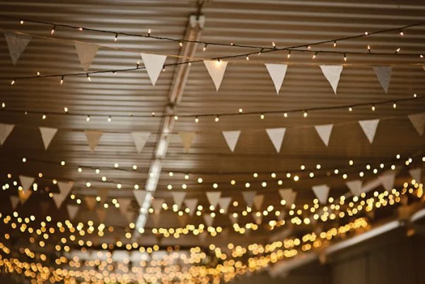 Ambiance chaleureuse et romantique avec des cordes de lumières et des triangles blancs suspendus au plafond.