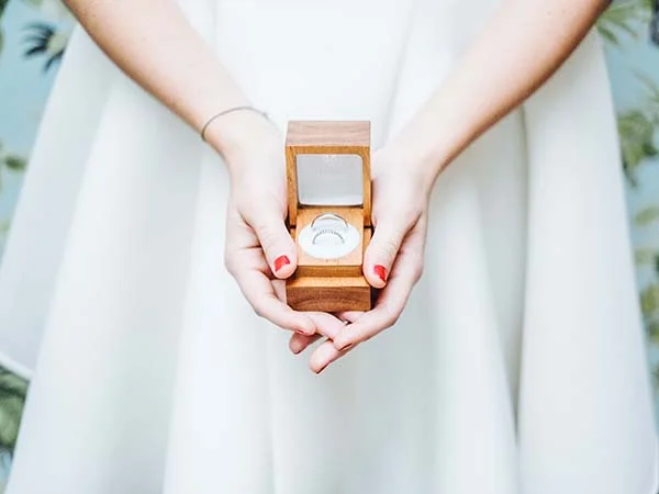 Main tendue tenant un boîte en bois avec une bague de mariage, idée romantique pour cacher votre baguette de mariage.