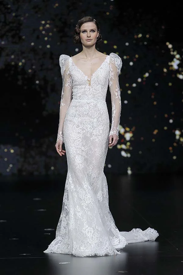 Modele exquis dans un manteau de mariage blanc intricément brodé, avec manches longues et train, défilant sur le podium.