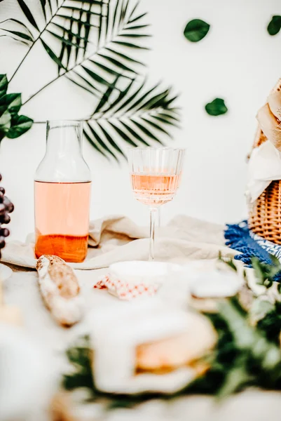 Évocation d'un repas romantique avec un verre de vin rose et des délicieux petits plats, décoré de feuilles vertes et de fleurs.
