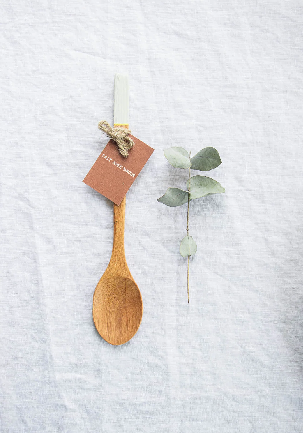 Un couteau en bois avec une étiquette "fait avec amour" et une branche de feuilles vertes, idéal comme cadeau