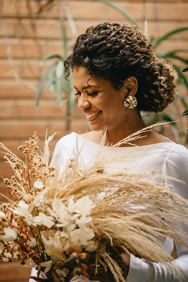 Élégante mariée tenant un bouquet de fleurs blanches, souriant dans un décor intérieur chaud et accueillant.