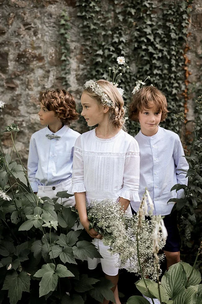 Élégance rurale et innocence d'un groupe d'enfants lors d'un mariage, entourés de végétation luxuriante et de fleurs blanches.