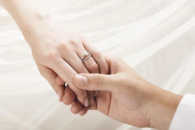 Une main tendue vers l'autre, l'union symbolique représentée par des anneaux de mariage.
