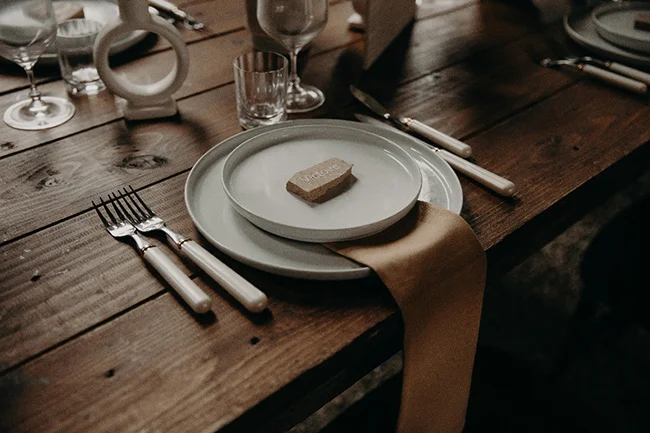 Dressage de table chic sur bois brut avec assiettes blanches, couverts minimalistes et serviette beige.