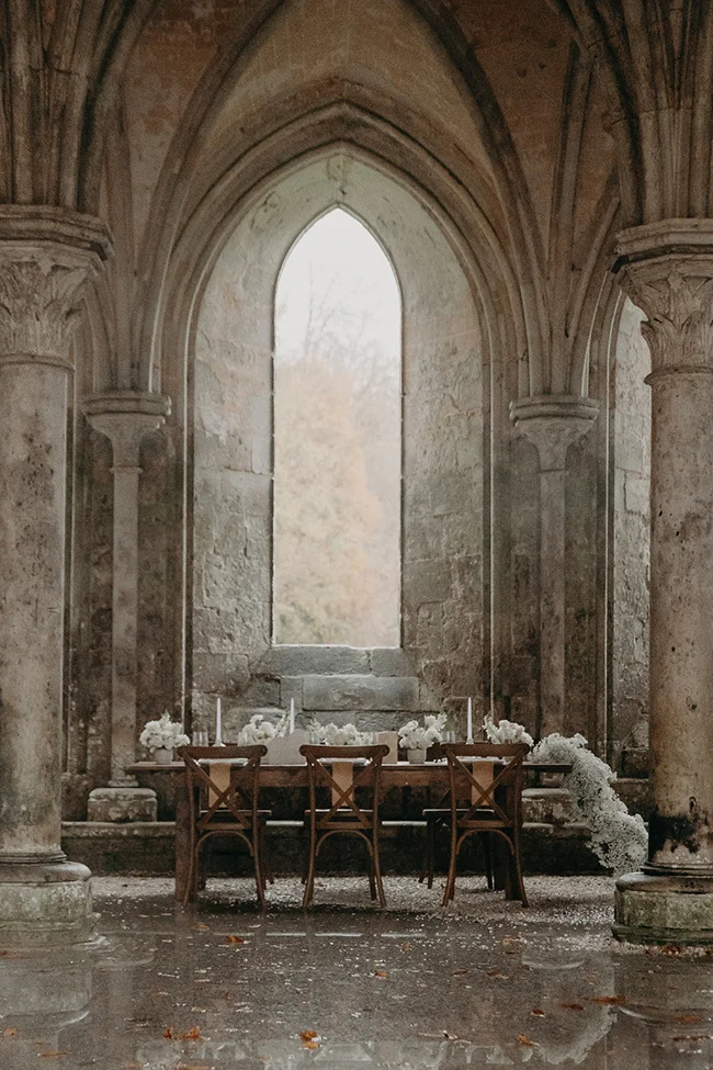 Table de mariage élégante avec fleurs blanches dans une abbaye en pierre aux tons neutres et ambiance romantique.