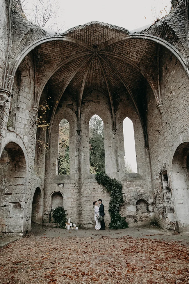 Couple de mariés s'enlaçant dans les ruines d'une abbaye en pierre aux tons neutres et ambiance romantique.