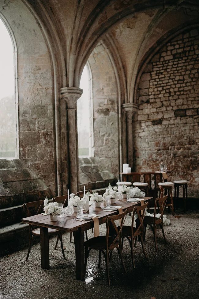 Table de mariage élégante avec fleurs blanches dans une salle voûtée en pierre aux tons neutres et romantiques.