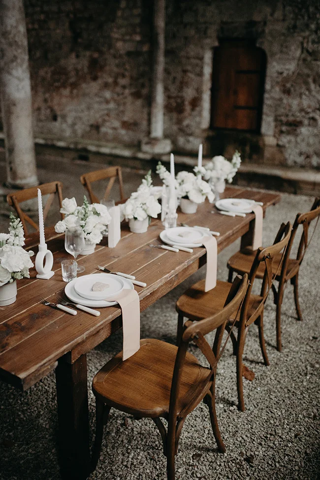 Table en bois rustique dressée avec des fleurs blanches et des bougies pour un dîner de mariage chic et épuré.