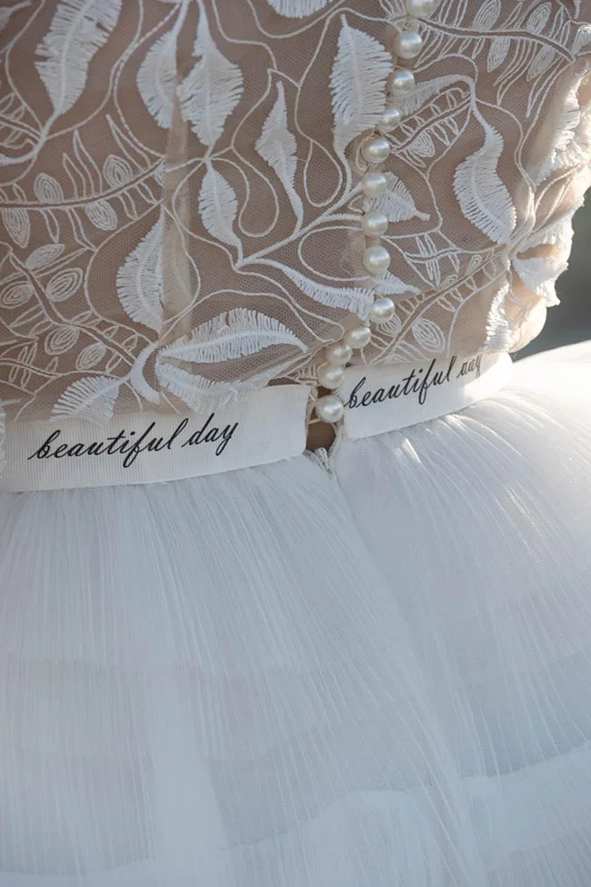 Détail d'une robe de mariée blanche en dentelle et tulle avec perles et ruban marqué beautiful day.