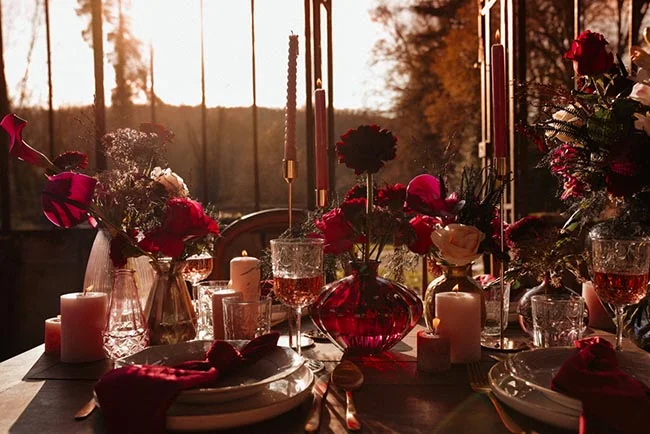 Table élégante aux tons rouge profond et or, éclairée par des bougies dans une ambiance romantique et contrastée.